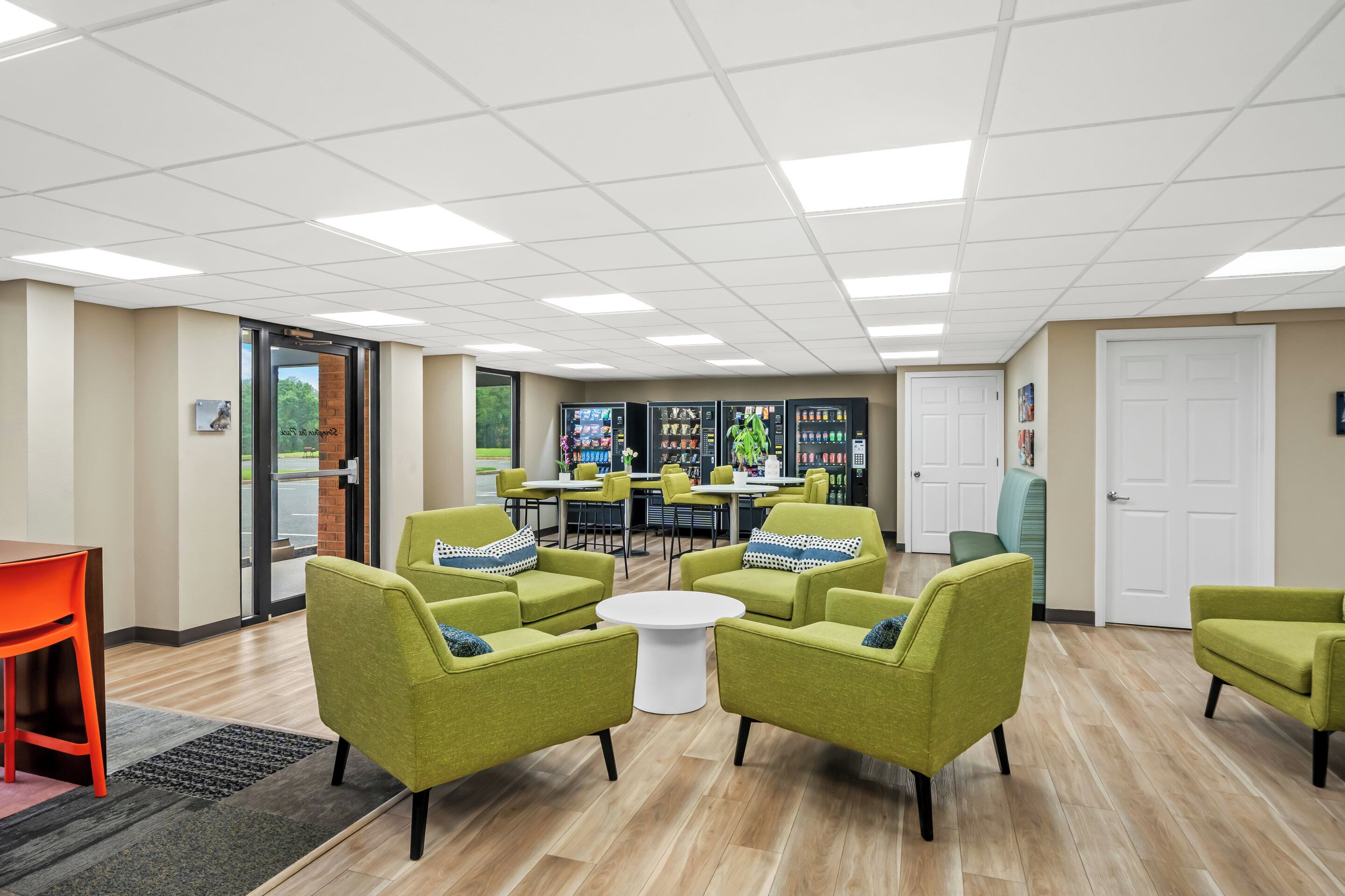 A modern lounge area with green armchairs, a white coffee table, and a vending machine.