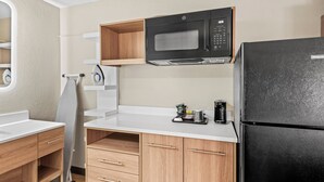 A compact kitchen with a black refrigerator, a microwave, and wooden cabinets. - Red Roof Inn Perryville (Perryville)