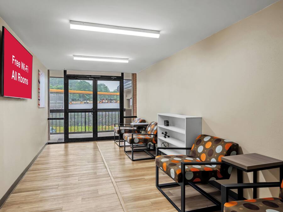 Una habitación de hotel moderna con suelo de madera, un ventanal con vistas al exterior, un televisor de pantalla plana en la pared y una zona de estar con una mesa consola blanca y sillas.