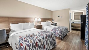 A hotel room with two beds, a desk, a chair, a desk lamp, a wall-mounted TV, and a refrigerator. - Red Roof Inn Perryville (Perryville)