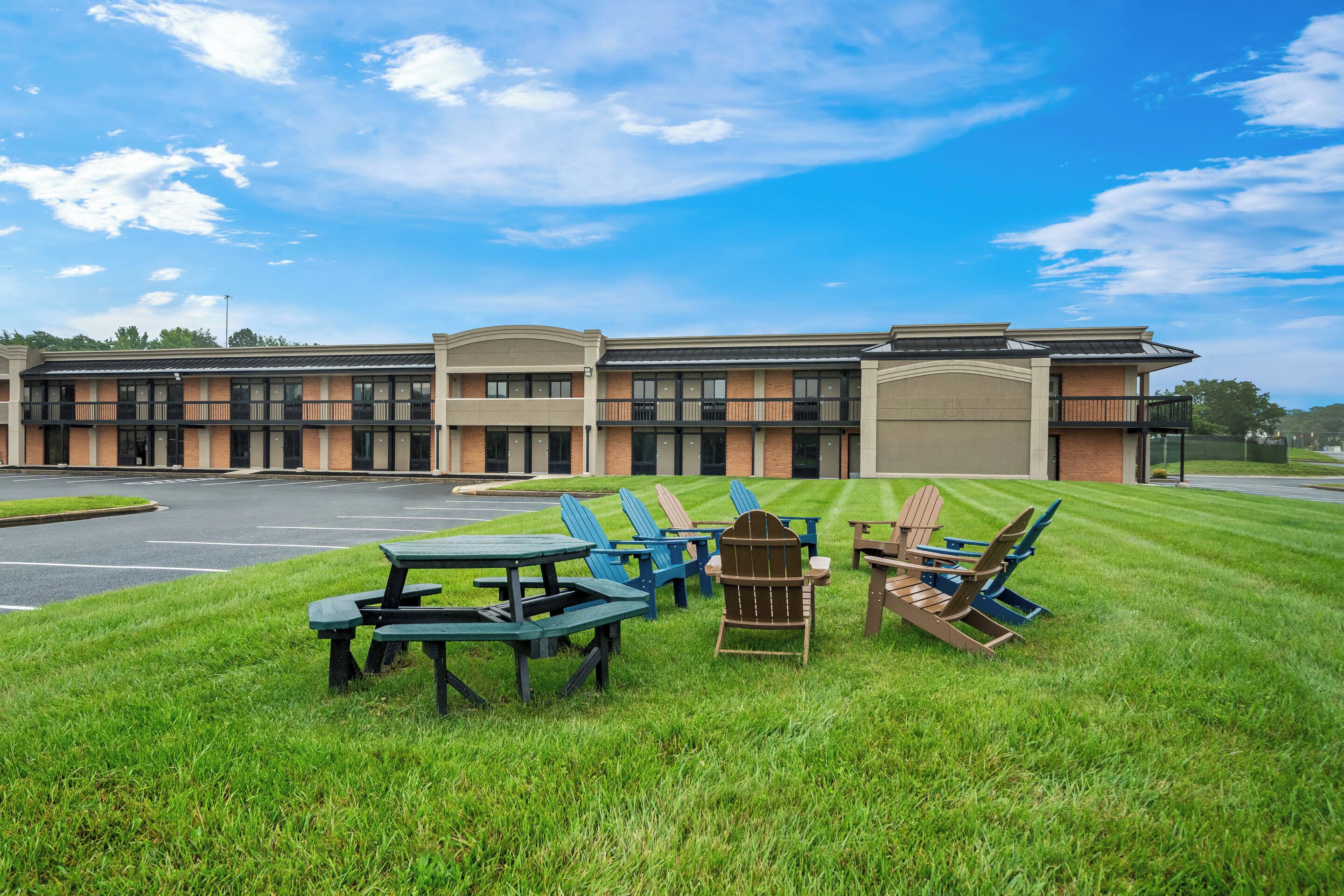 A building with a parking lot and outdoor seating area with tables and chairs.