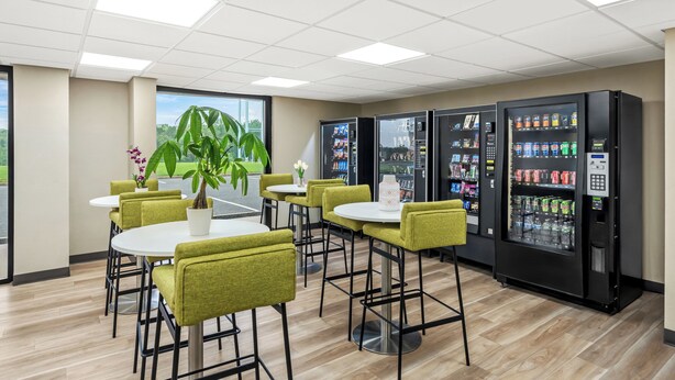 A modern indoor space with round tables and green chairs, vending machines, and a large potted plant. - Red Roof Inn Perryville (Perryville)