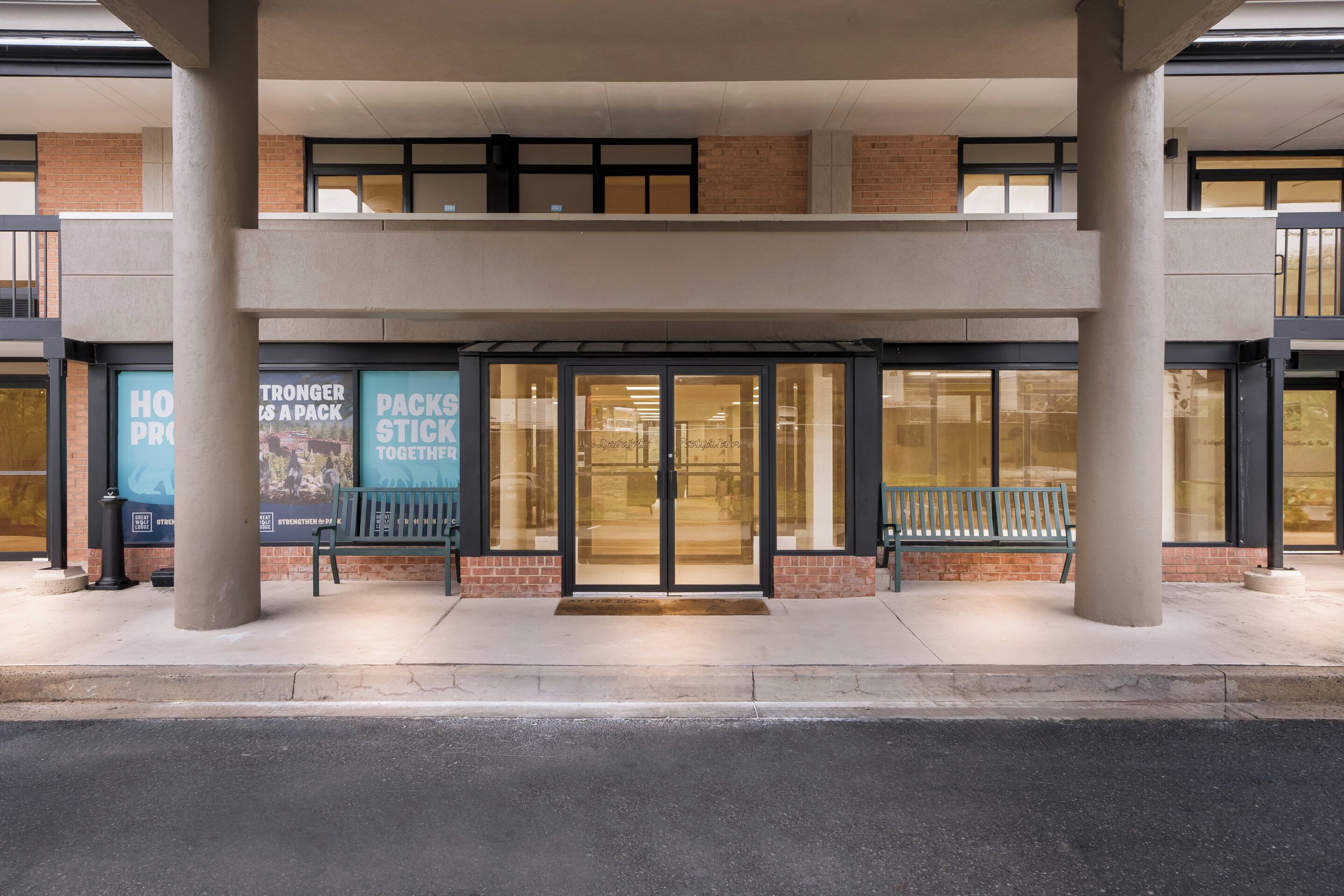 A building entrance with glass doors, a bench, and a sign that reads "STRONGER PACKS STICK TOGETHER".