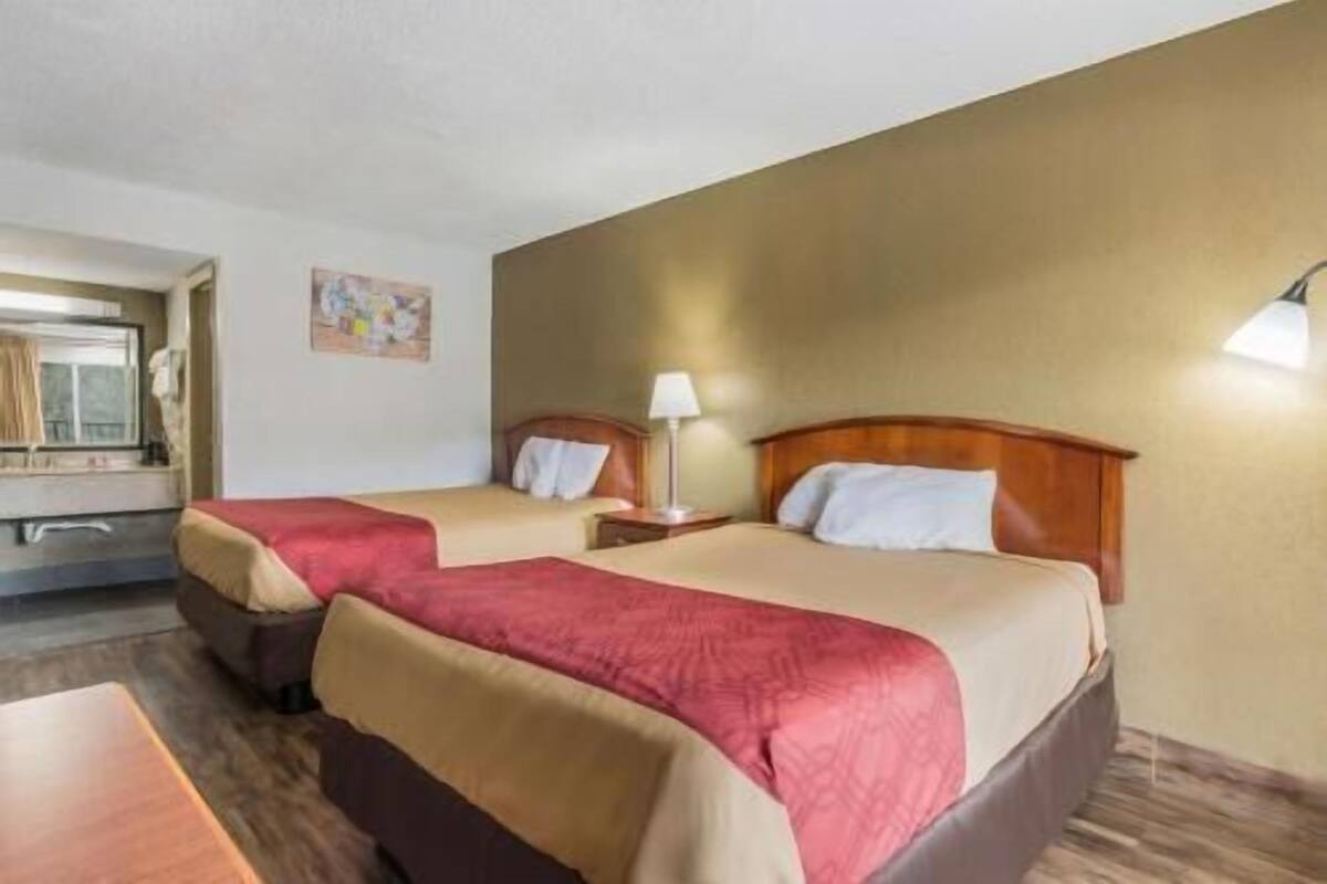 A hotel room with two beds, a desk, a lamp, and a painting on the wall.