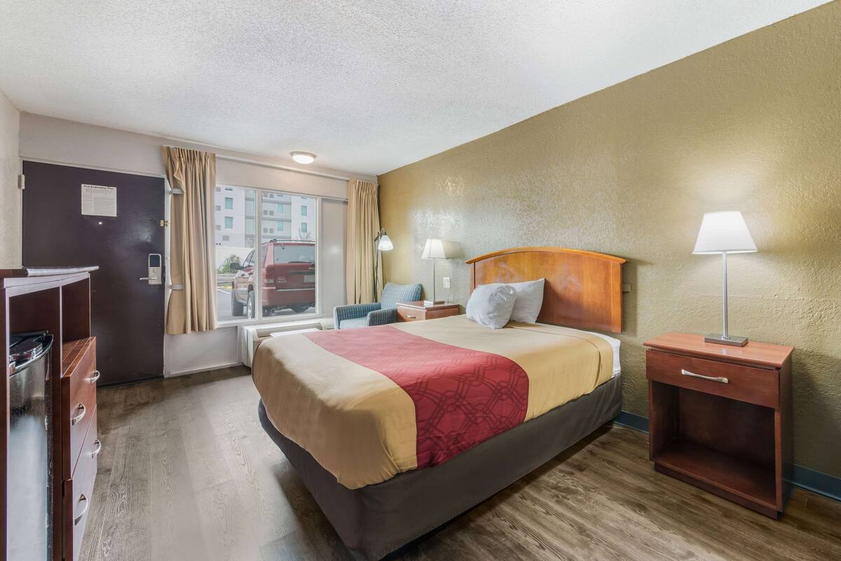 A hotel room with a bed, bedside tables, a desk, a chair, and a window with curtains.