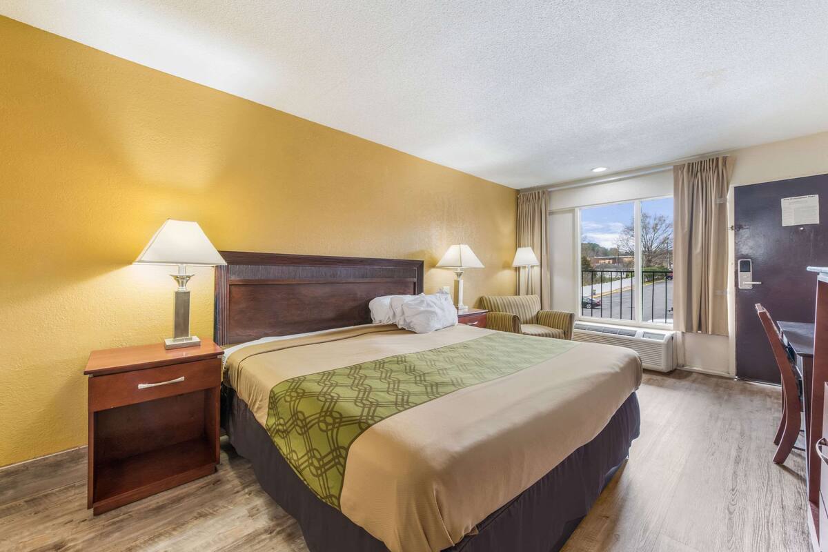 A hotel room with a large bed, two bedside tables with lamps, a window with curtains, and a view of the outside.