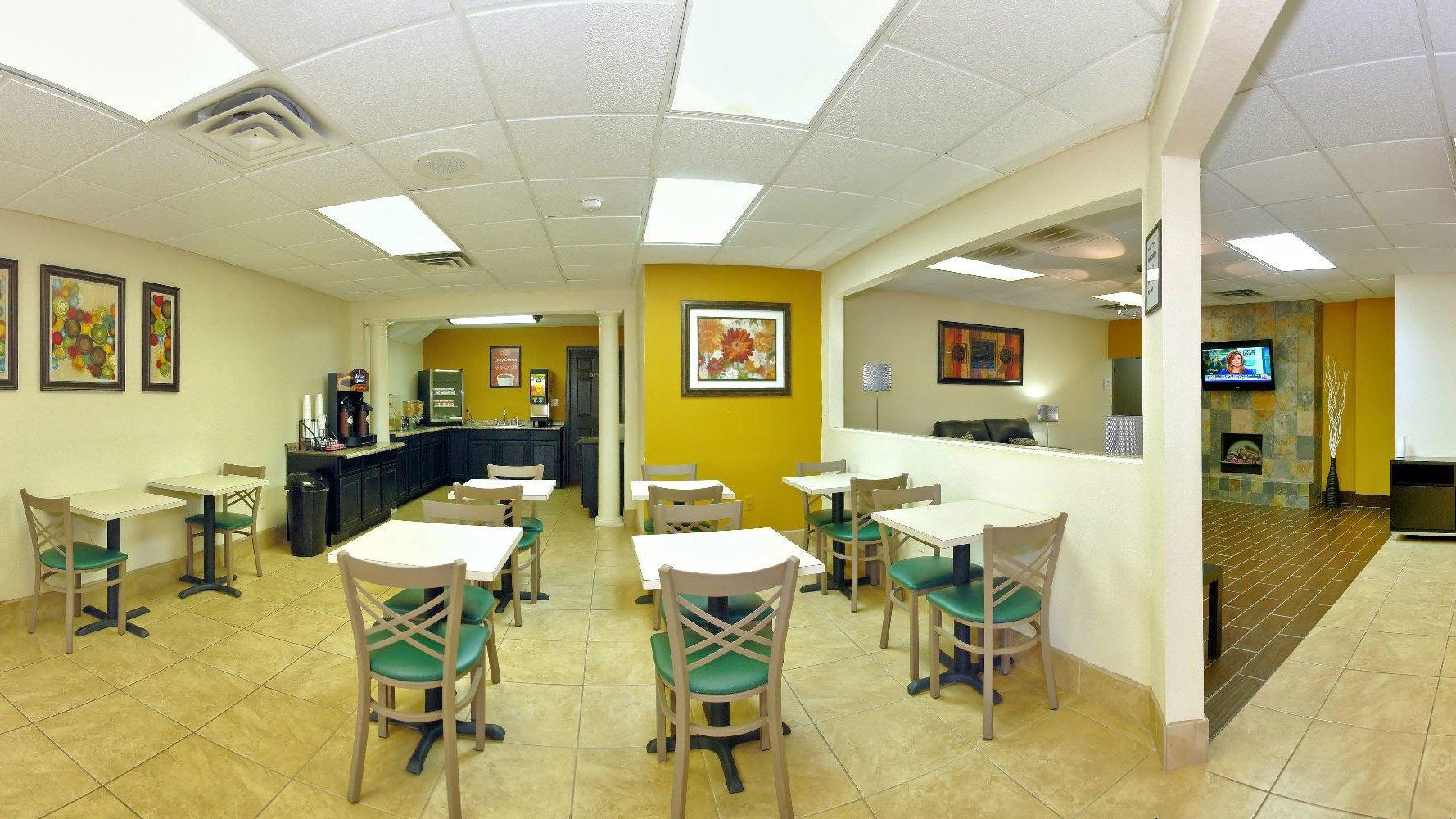 A restaurant with multiple tables and chairs, a counter, and a television mounted on the wall.