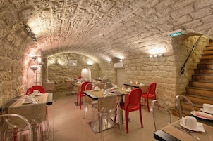 A stone-walled dining area with tables and chairs, a staircase, and a view of another room.