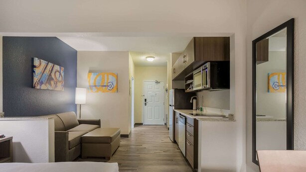 A hotel room with a bed, a sofa, a kitchenette, and artwork on the walls. - MainStay Suites Joliet I-80 (Joliet)