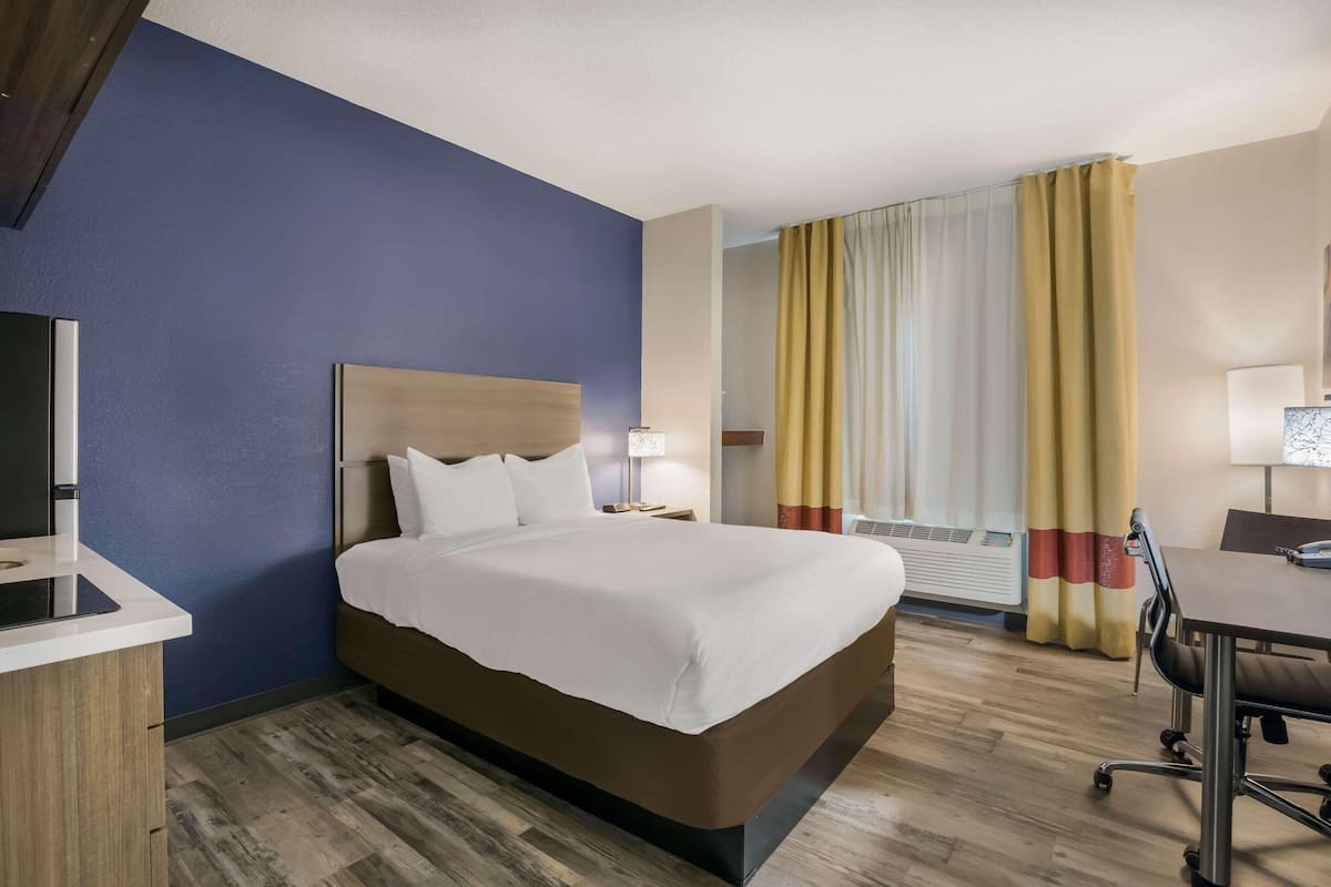 Una camera d'albergo con un letto, un comodino, una lampada e una scrivania con una sedia.