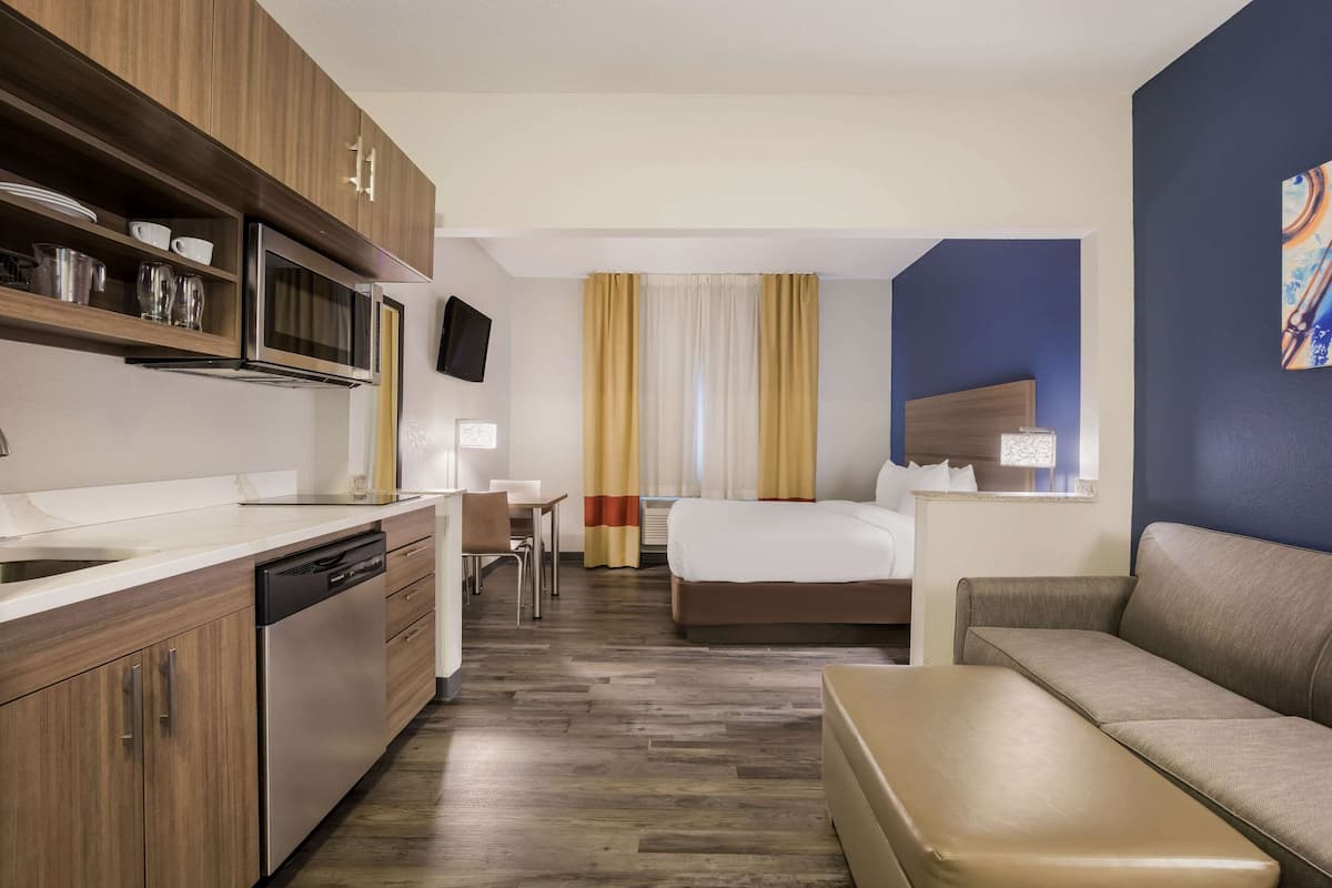 Una camera d'albergo con angolo cottura, un letto, un divano e un tavolino.