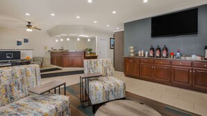A modern living room with a sofa, armchair, and coffee table, a kitchen area with wooden cabinets and a flat-screen TV, and a ceiling fan. - MainStay Suites Joliet I-80 (Joliet)