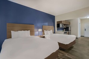 A hotel room with two beds, a kitchenette, and a door leading to another room.