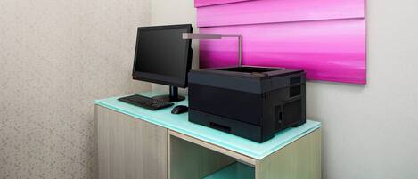 Ein Schreibtisch mit Computermonitor und Drucker, ein Türkis-Schreibtisch sowie eine Wand mit Farbverlauf-Kunstwerk.