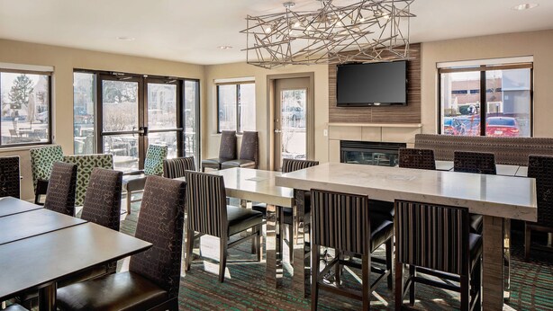 A modern hotel dining area with a large rectangular table, multiple chairs, a fireplace, and a flat-screen TV mounted on the wall. - Residence Inn by Marriott Denver Tech Center (Greenwood Village)