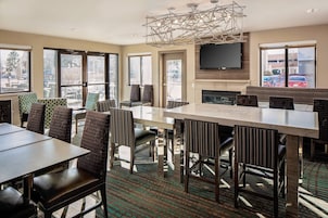 Un comedor de hotel moderno con una gran mesa rectangular, varias sillas, una chimenea y un televisor de pantalla plana montado en la pared.