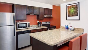 A kitchen with a stainless steel refrigerator, a microwave, a coffee maker, and a stove. There is a granite countertop and a small island with two red chairs. - Residence Inn by Marriott Denver Tech Center (Greenwood Village)