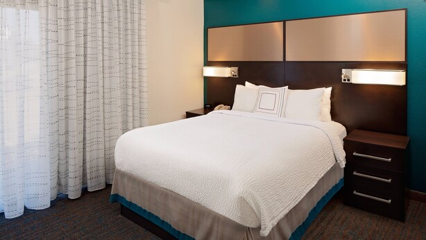 A hotel room with a large bed, a nightstand, and a headboard with built-in lighting.
