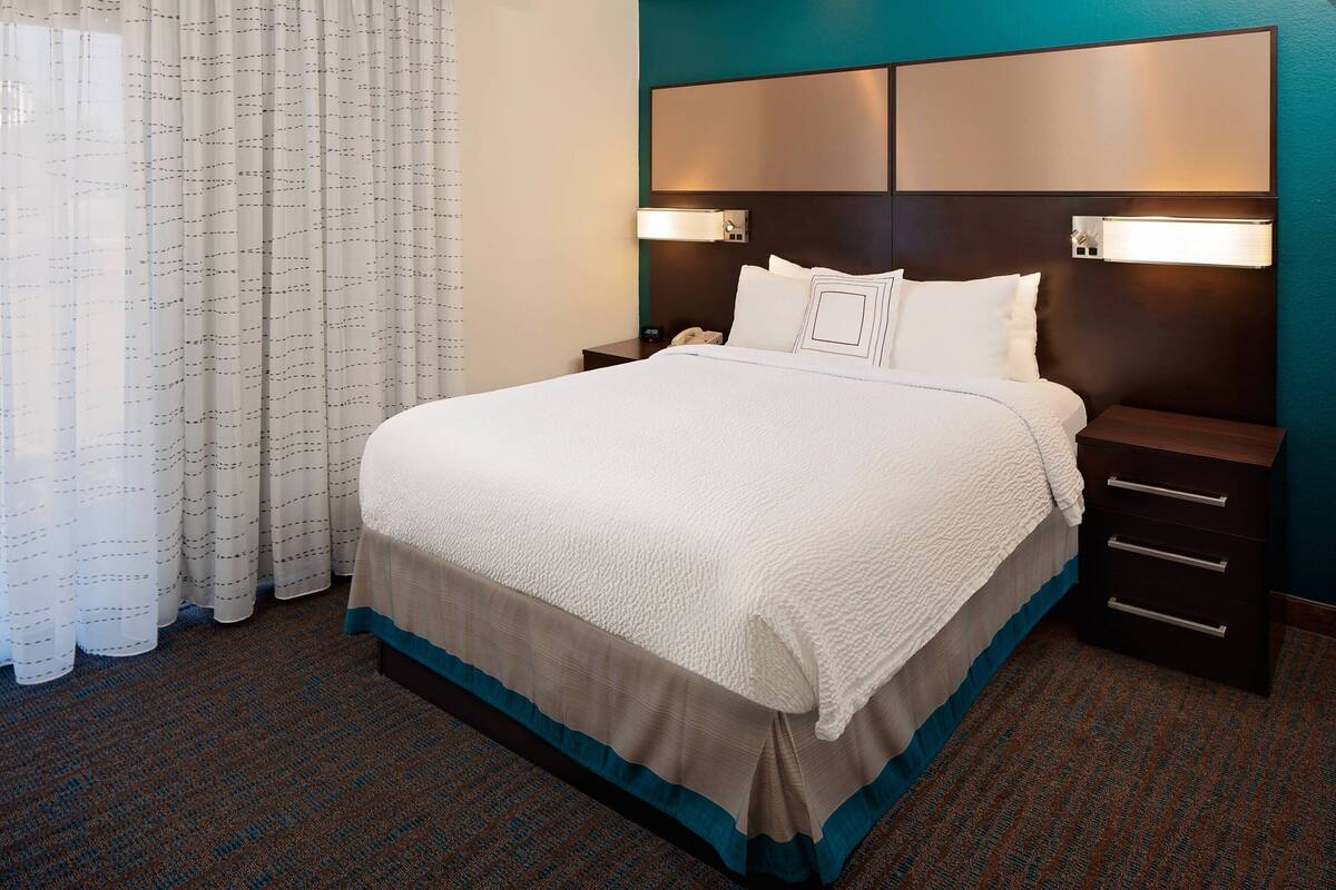 A hotel room with a large bed, a nightstand, and a headboard with built-in lighting.
