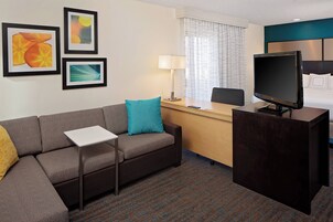 Una habitación de hotel con sofá, escritorio, televisor y cuadros en la pared.