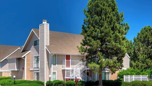 A two-story building with a central staircase, a balcony on the upper floor, and a well-maintained lawn with a large pine tree.