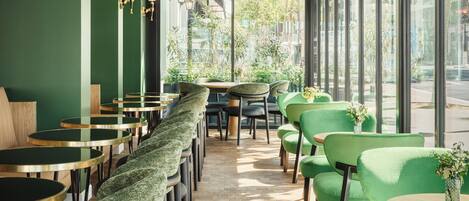 Un café moderno con sillas y mesas verdes, ventanas amplias y suelo de madera.