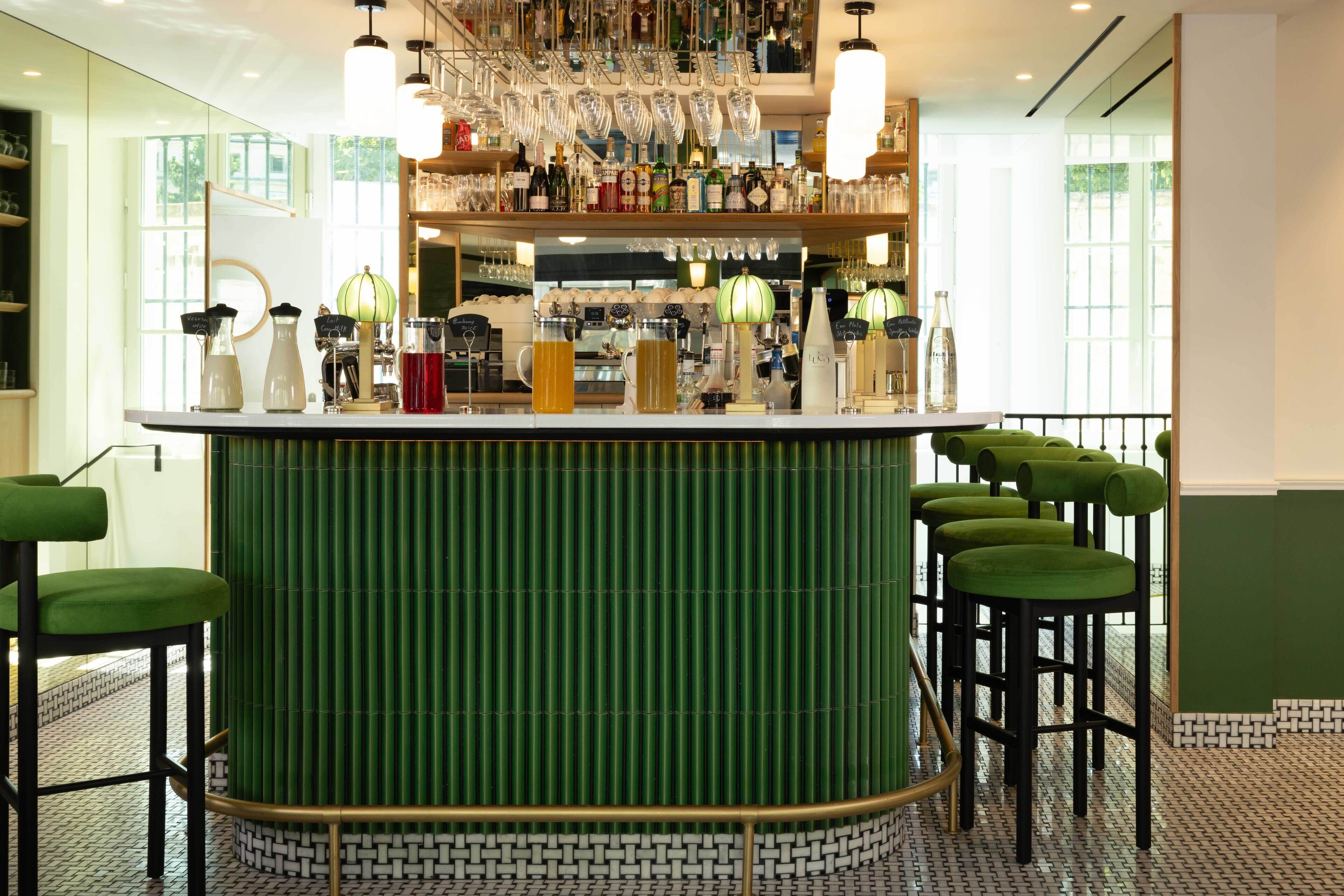 A bar area with a green bar counter, multiple stools, and a variety of bottles and glasses.