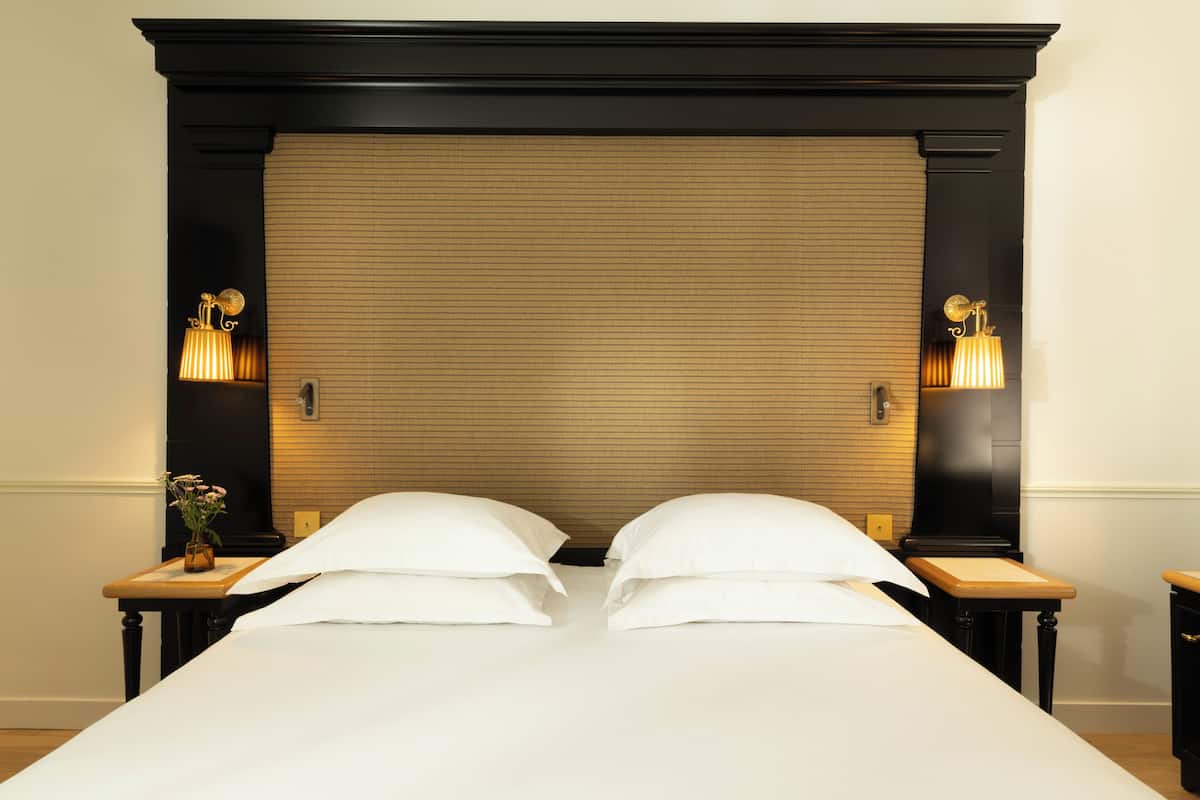 A double bed with a wooden headboard, two bedside tables, and wall-mounted lamps.
