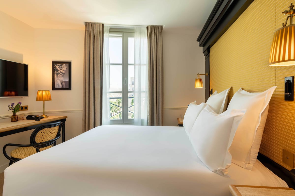A hotel room with a large bed, a desk with a lamp, a television, and a window with curtains.