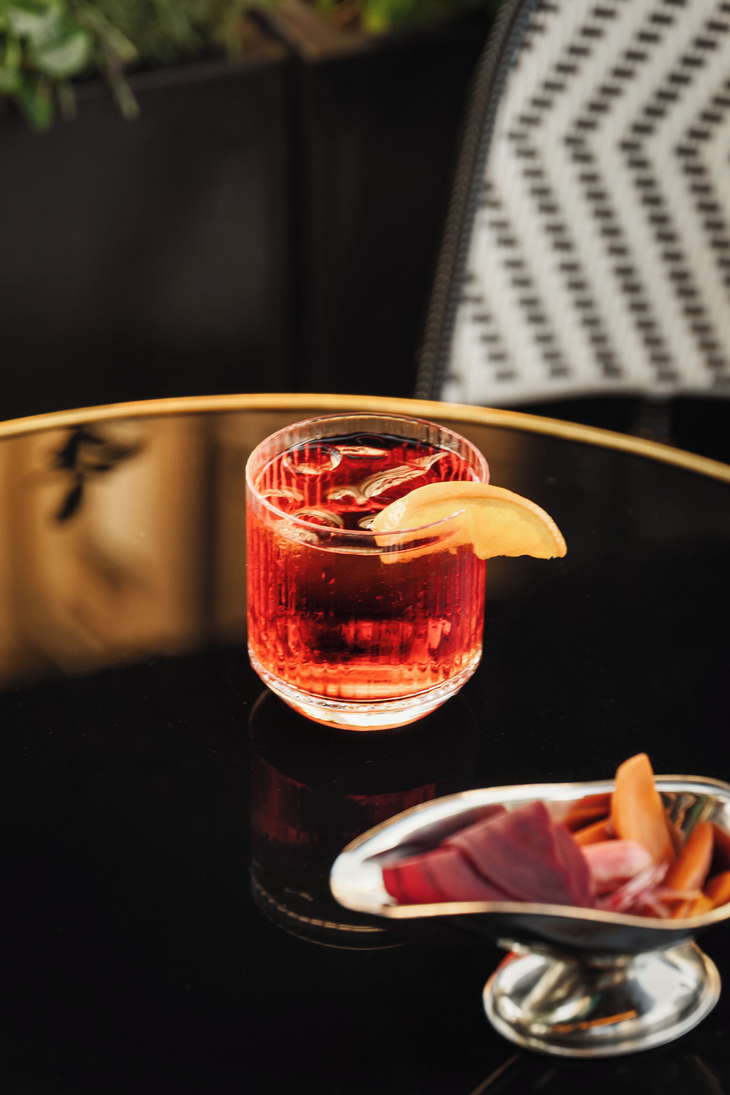 Un vaso de bebida roja con una rodaja de limón sobre una mesa negra reflectante.