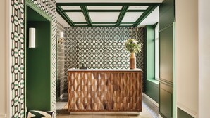 A reception area with a patterned wall, a wooden reception desk, and a green accent wall. - Hôtel Observatoire Luxembourg (Paris)