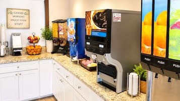 Eine Selbstbedienungs-Getränkestation mit Auswahl an Kaffee, Saft und Wasser, sowie ein Schild mit der Aufschrift 'GOOD MORNING ENJOY YOUR STAY!'