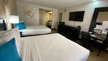 Habitación de hotel con dos camas, un escritorio, una silla, un televisor y un espejo.