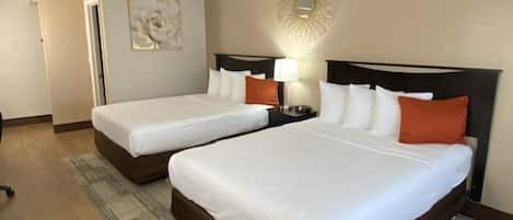 Habitación de hotel con dos camas, una mesita de noche con lámpara, un adorno en la pared y una puerta que da a otra habitación.