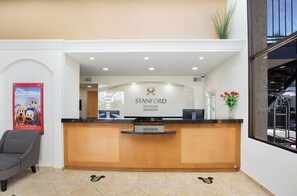 Taulell de recepció amb un cartell de Stanford Inn & Suites Anaheim, un pòster de Disney California Adventure i una cadira a l'esquerra.