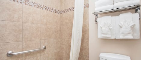 A bathroom with beige tiles, a shower curtain, a grab bar, a towel rack with folded towels, and a toilet.