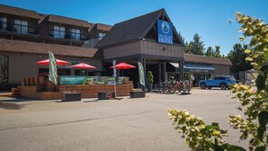Un hotel con un letrero llamativo, mesas al aire libre con sombrillas rojas y un punto de alquiler de bicicletas.