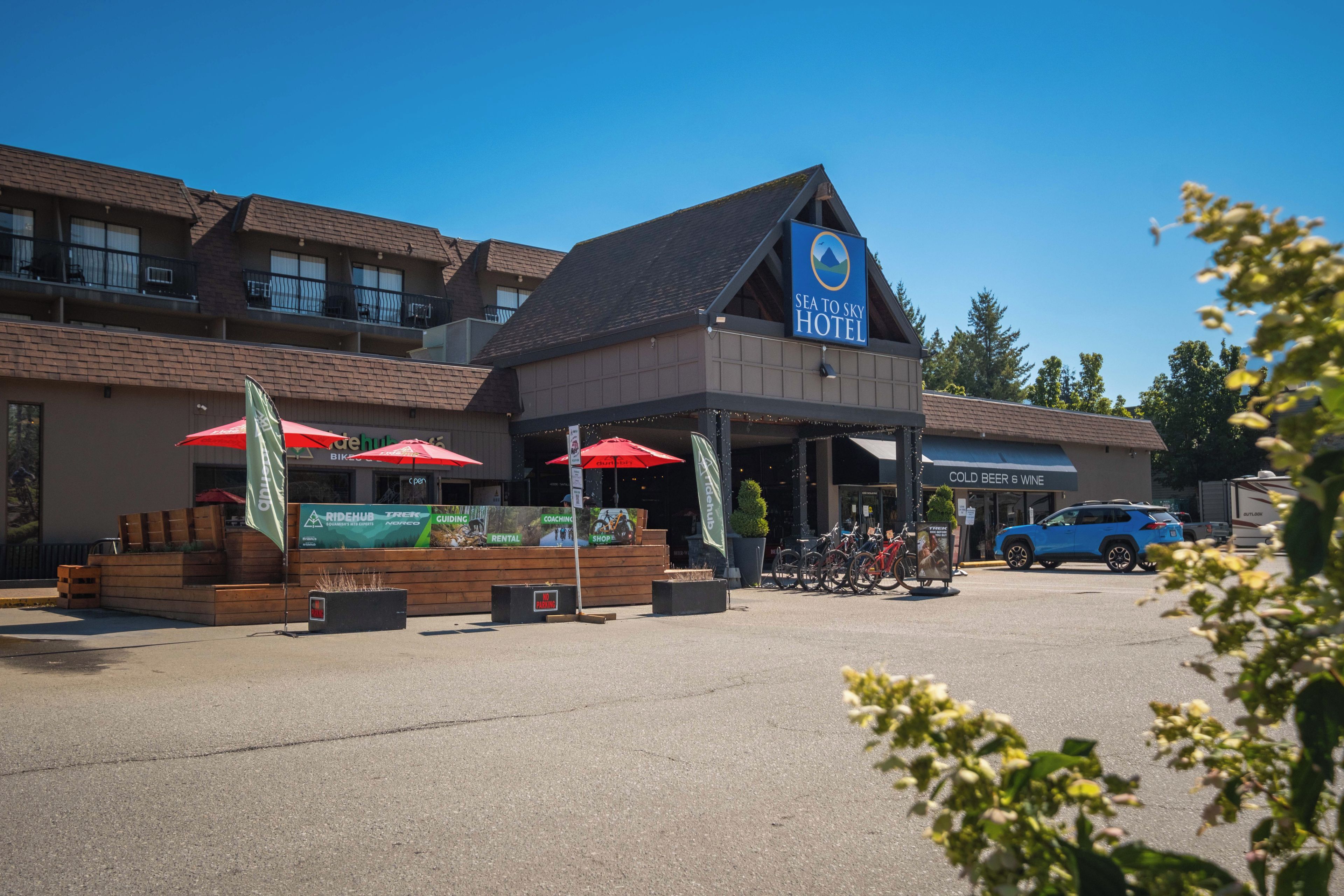 A hotel with a prominent sign, outdoor seating with red umbrellas, and a bike rental station.