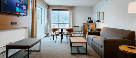 Una habitación de hotel moderna con una televisión de pantalla plana, un sofá, una mesa de centro, un banco y un comedor con sillas.
