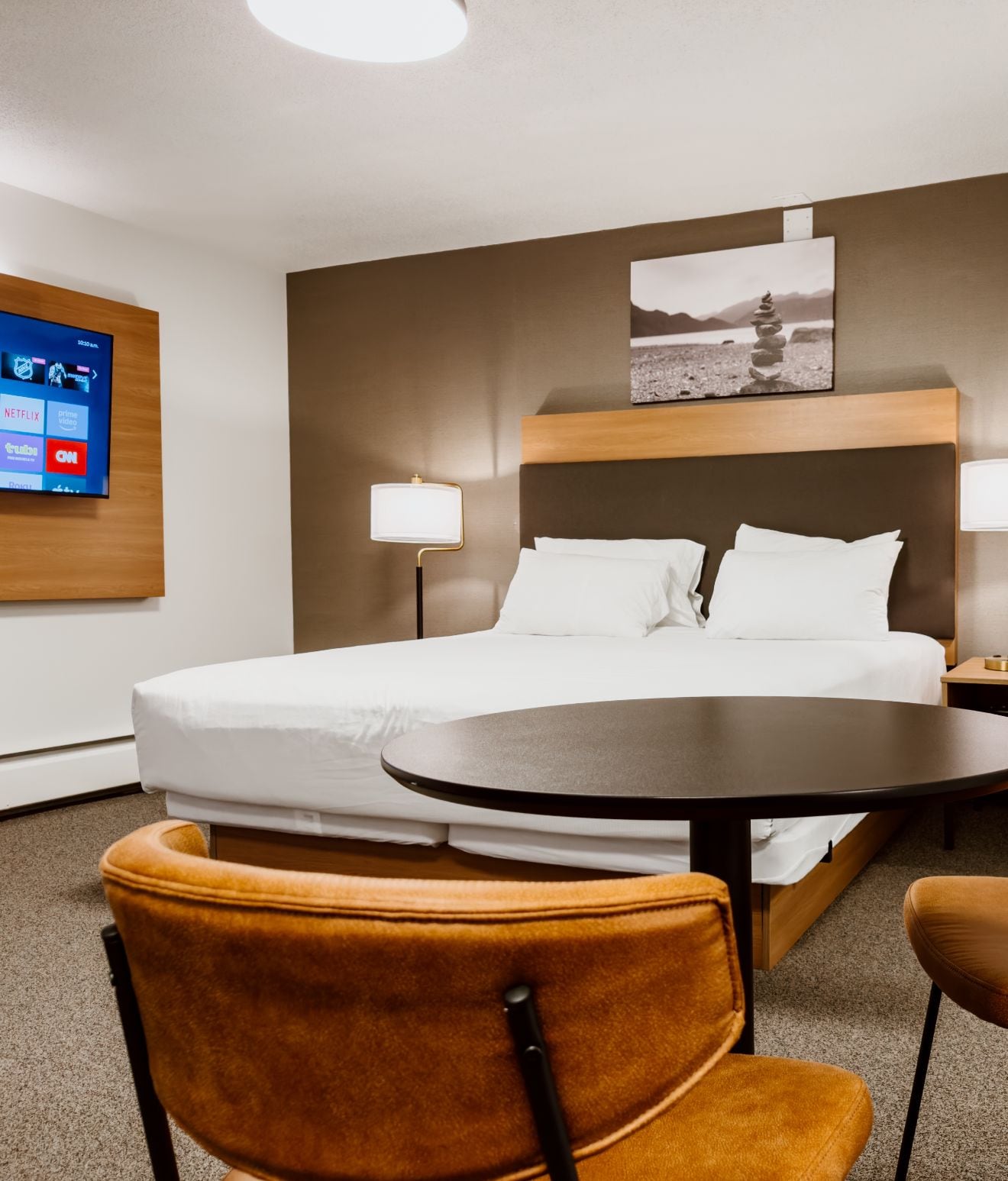 A hotel room with a bed, bedside lamps, a flat-screen TV, and a painting on the wall.