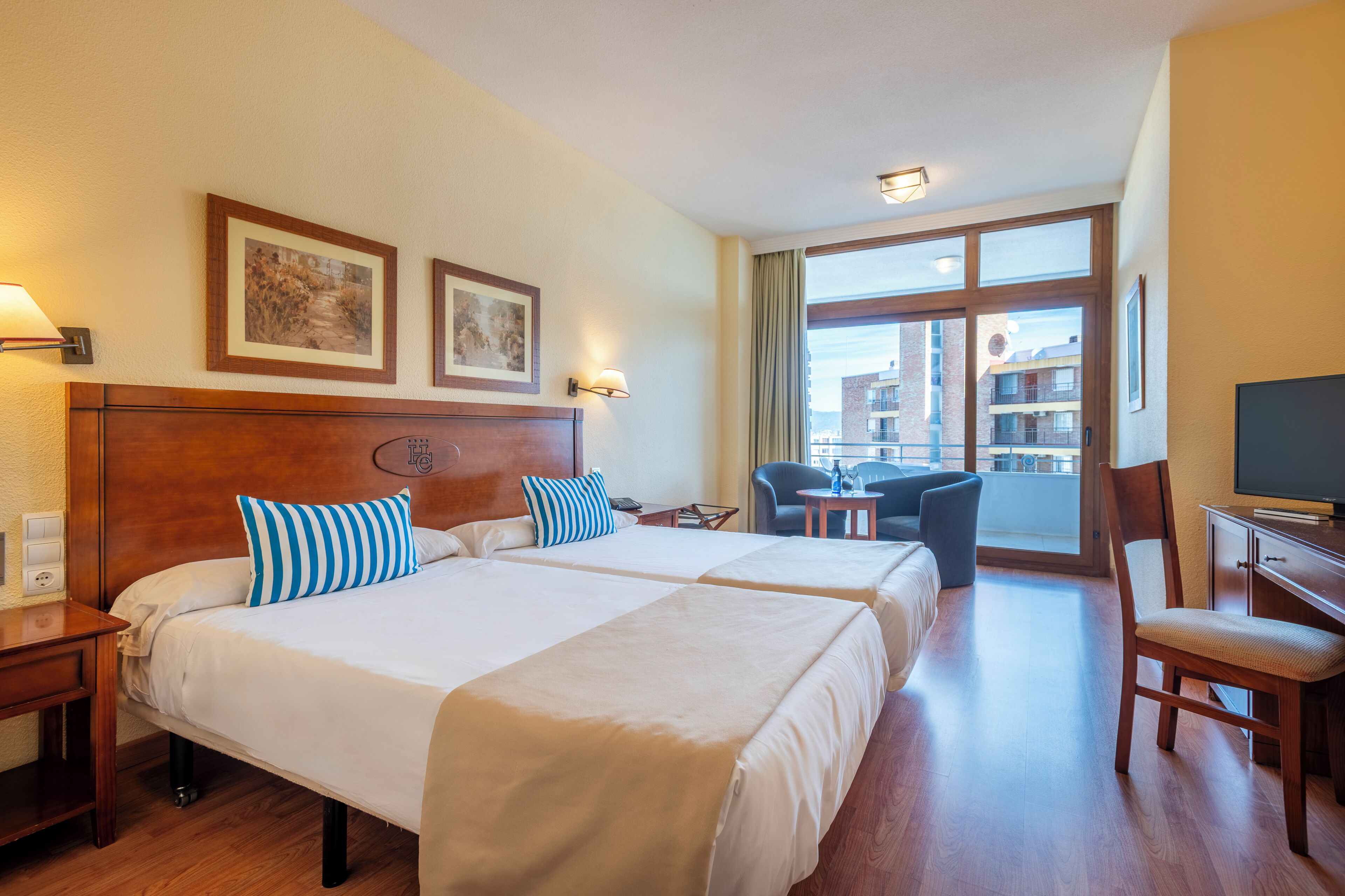 A hotel room with two beds, a desk, a chair, a television, and a balcony with a view.