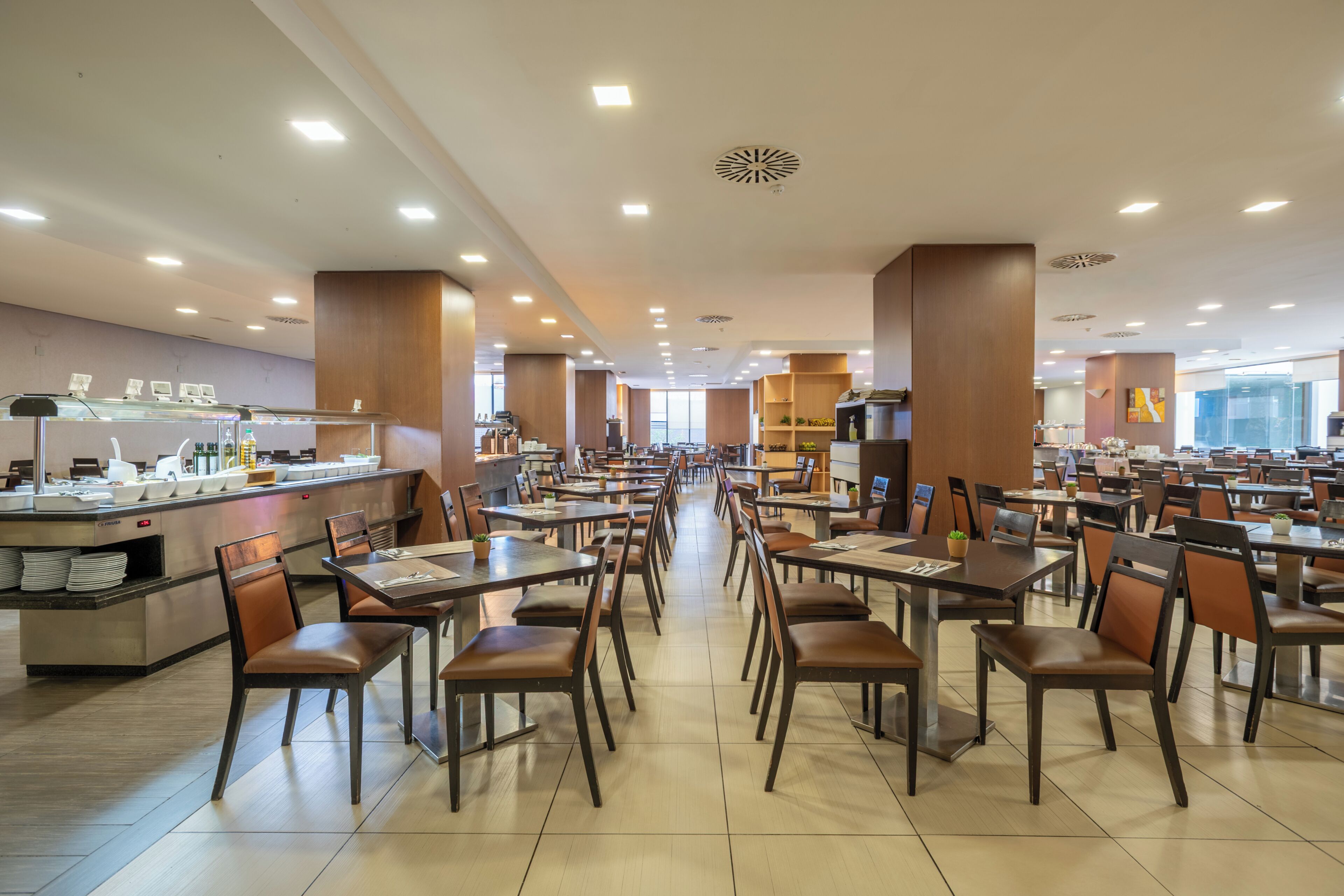 A spacious dining area with multiple tables and chairs, a buffet counter, and a view of the outdoors.