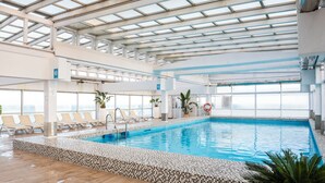 An indoor swimming pool with tiled flooring, lounge chairs, and potted plants. - Leonardo Hotel Torremolinos Costa del Sol (Torremolinos)