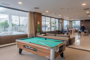 A pool table in a modern indoor space with large windows, a seating area, and a view of the outside.