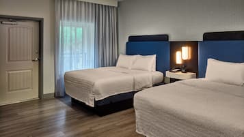 Une chambre d’hôtel avec deux lits, une porte, une fenêtre avec des rideaux, une table de chevet avec une lampe et un mur décoré d’un motif.