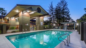 Une piscine dotée d’une zone couverte, un bâtiment avec un toit en tuiles et un jardin clos.
