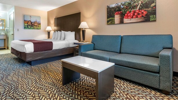 Une chambre d’hôtel avec un lit, un canapé bleu, une table basse, deux lampes de chevet et deux tableaux au mur.