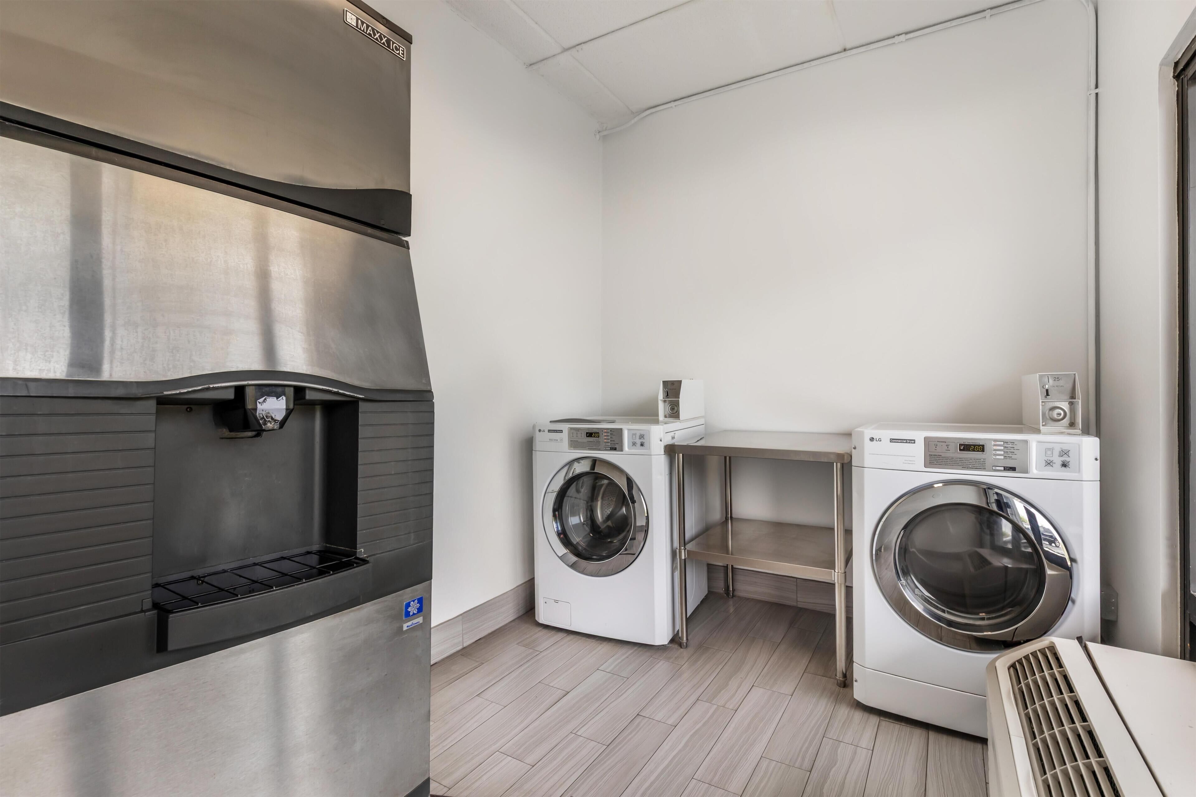 A laundry room with a stainless steel refrigerator, two white LG washing machines, and a small shelf.