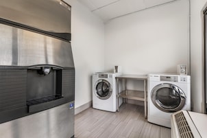 A laundry room with a stainless steel refrigerator, two white LG washing machines, and a small shelf.