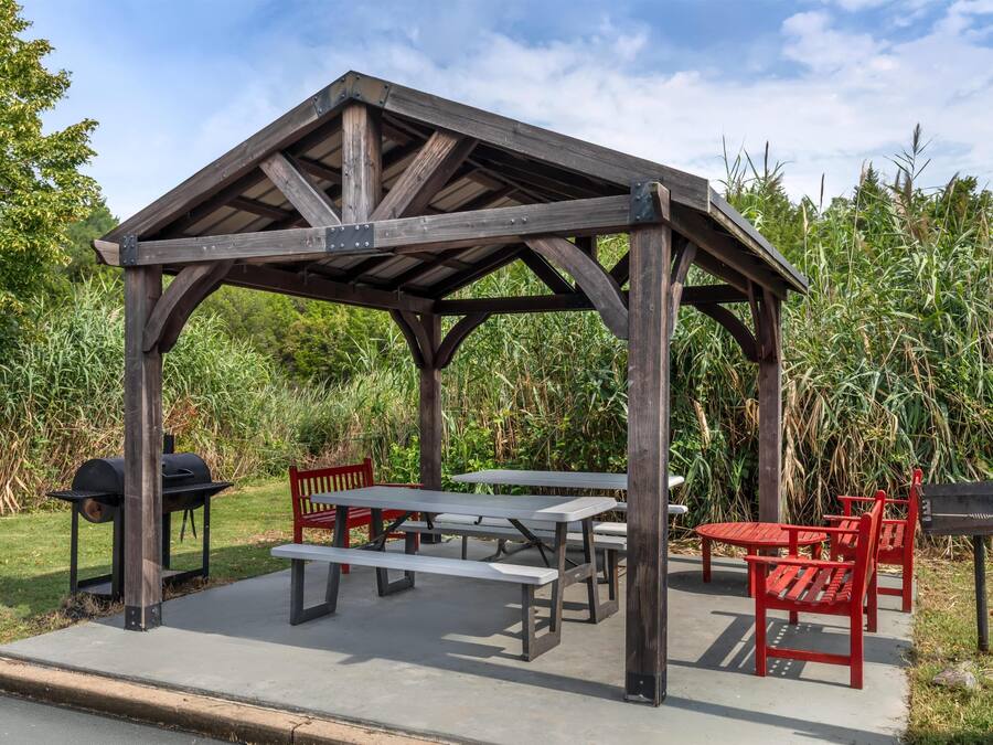 A wooden pavilion with picnic tables and benches, a grill, and a red bench.